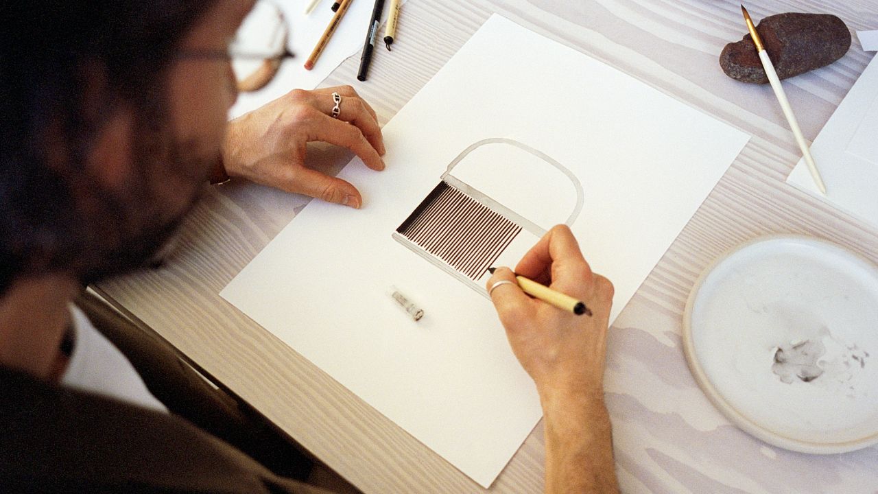 Designer fra B&O sidder ved et skrivebord, og tegner et nyt produkt på et A4-papir, der illustrerer Bang & Olufsens fokus på high-end design