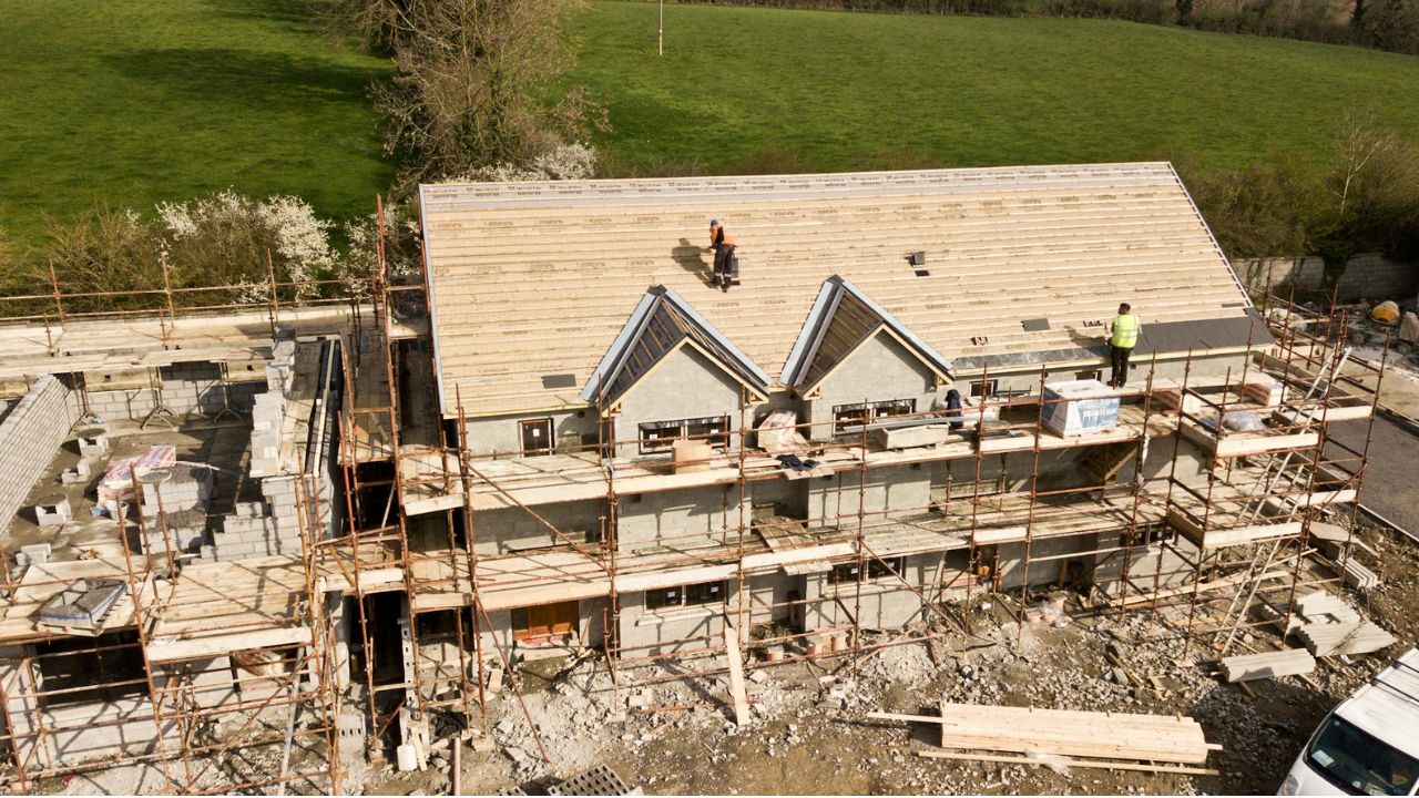 Hus under opbygning på en villavej, hvor håndværkere udfører forskellige arbejdsopgaver, symboliserer HusCompagniets økonomiske vækst og kommende børsnotering