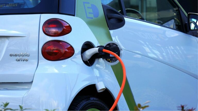 Bagenden af en lille hvid elbil fra den danske delebilstjeneste GreenMobility, der oplader på en parkeringsplads