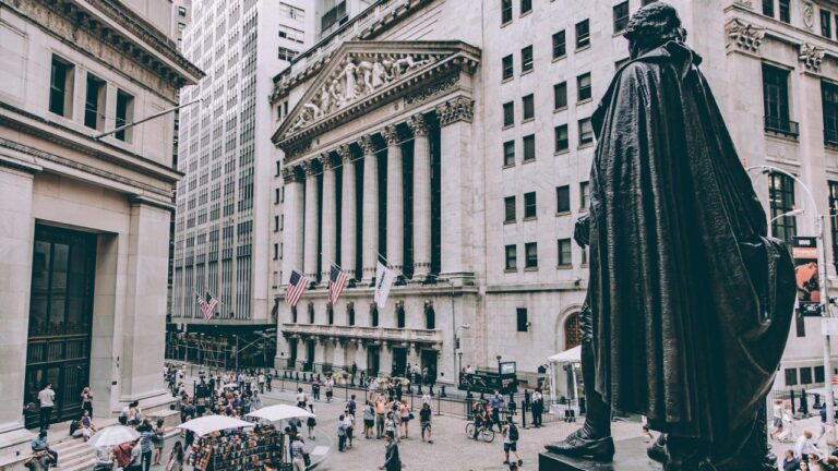 Bronzestatue af USA's første præsident, George Washington, ser ud over Wall Street, mens folk går og cykler foran New York Stock Exchange, hvilket symboliserer betydningen af de største og mest velkendte børser i verden