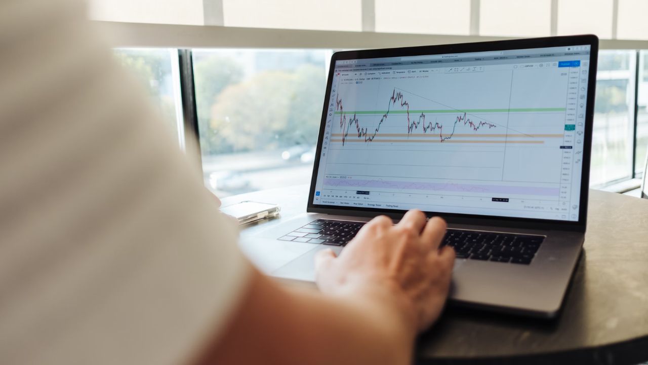 Mand sidder ved et rundt bord med en Macbook, hvor skærmen viser et aktiediagram, hvilket symboliserer Fear & Greed Index og dets indflydelse på markedet