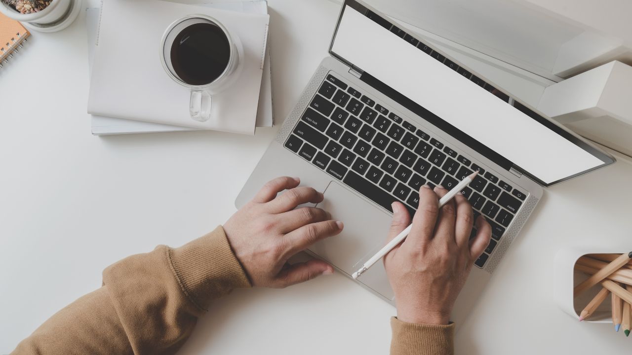 Person sidder ved et skrivebord med en kop kaffe og arbejder på sin computer, hvilket symboliserer muligheden for at tjene penge hjemmefra